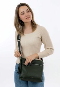 Dark green leather crossbody bag with a textured finish, featuring a zippered pocket and a tassel detail on the side.