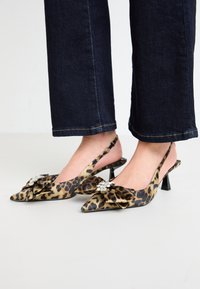 Cipele na petu s uzorkom leoparda, otvorene s gležnja, s oštrim vrhom, gornji dio od tkanine, dekorativna mašna i dragulj na vrhu. Crni stiletto potplat.