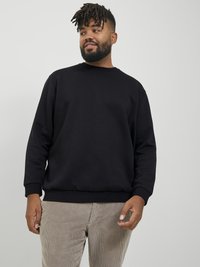 Black crewneck sweatshirt with long sleeves and ribbed cuffs, paired with light corduroy pants; relaxed fit and smooth texture.