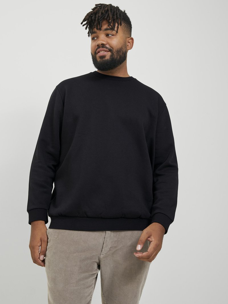 Black crewneck sweatshirt with long sleeves and ribbed cuffs, paired with light corduroy pants; relaxed fit and smooth texture.