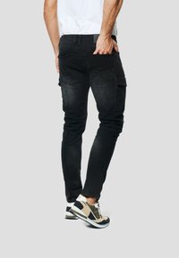 Čierne cargo nohavice so štíhlym strihom, štyrmi vreckami a mierne vyblednutou textúrou. Kombinované so športovými teniskami v béžovej farbe s čiernymi detailmi.