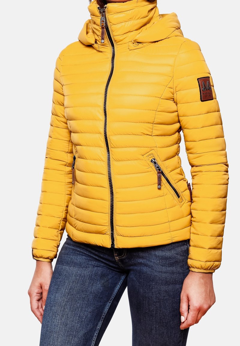Veste matelassée jaune avec fermeture éclair à l'avant, poches latérales zippées et capuche, portée avec un jean bleu foncé sur une personne.