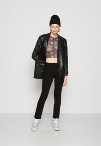 Sacou oversized din piele neagră, top scurt transparent gri cu model în formă de inimă, pantaloni skinny negri și teniși albi cu accente negre. Beanie negru.
