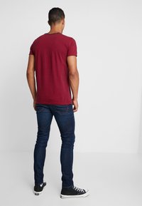 Camiseta de manga corta con rayas rojas y azul marino, combinada con vaqueros de mezclilla azul oscuro y zapatillas negras de caña alta. La tela parece suave, diseño ajustado.