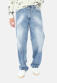 Jeans azzurri chiari, con un design a gamba dritta, caratterizzati da un lavaggio sbiadito, cinque tasche e chiusura a bottone. Indossati con scarpe da ginnastica bianche.