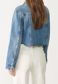 Ljusblå denimjacka med kort längd och långa ärmar, synlig söm och rå fåll. Kombinerad med vita högmidjade byxor.