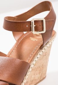 Sandalo con zeppa in pelle marrone, dotato di chiusura con fibbia, con tacco intrecciato in stile espadrille e superficie liscia opaca.