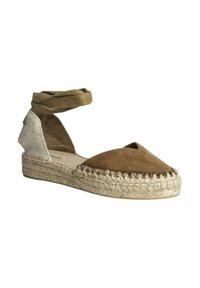 Espadrille de ante marrón con punta afilada, suela de yute y tira al tobillo. Presenta un panel de tejido trenzado y acentos texturizados.