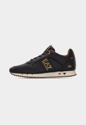 Schwarzer Ledersneaker mit goldenem EA7 Emporio Armani-Logo, braunem Innenfutter, weißer Sohle mit Profil und kleinem italienischem Flaggen-Detail nahe der Ferse.