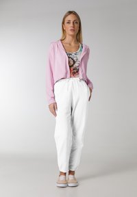 Lyserød cropped hoodie over en multicolor blomstret tanktop, parret med løse hvide joggerbukser og beige sneakers. Glat tekstur.