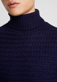 Granatowy sweter z golfem, wykonany z dzianiny, z teksturowanym wzorem i prążkowanym kołnierzem, uszyty z miękkiej, ciepłej tkaniny.