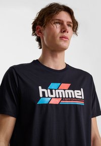 Granatowa bawełniana koszulka z krótkim rękawem, z dużym, kolorowym logo "hummel PERFORMANCE" z przodu. Gładka struktura.