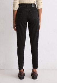 Czarny denimowy materiał, wysoki stan, dopasowany krój, dwa tylne kieszenie i gładka faktura. Noszone z brązowymi butami.