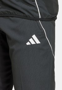 Schwarze Sporthosen aus leichtem Material besitzen eine dezente Textur, weiße Akzente und das Adidas-Logo, das prominent platziert ist.