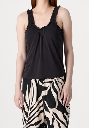 Femme portant un haut noir sans manches avec des bretelles volantées et un pantalon large noir et beige à motifs.