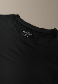 Fekete pamutpóló, kerek nyakkivágással. A belső címkén a "NEXT SIGNATURE M" felirat olvasható, amely a méretet és származást jelzi. Simább tapintású anyag.