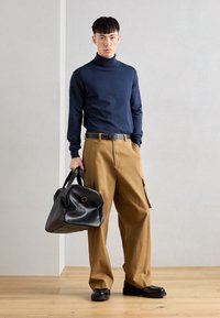 Mornarsko turtleneck pulover, široke bež cargo hlače, crni remen, crna kožna torba s okruglim rubovima i crne cipele.