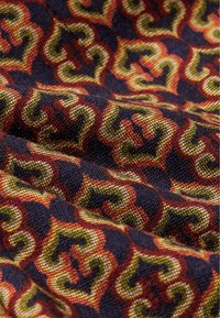 Bomullstyg med ett virvlande mönster i rött, gult och grönt mot en mörkblå bakgrund. Texturerad väv framhävt.