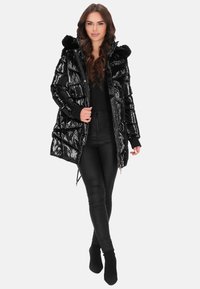 Fekete puffert kabát fényes felülettel, szőrmével bélelt kapucnival, cipzáras és patentos záródással, oldalzsebekkel és középmagas hosszúsággal. Fekete nadrággal viselve.