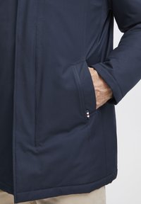 Chaqueta azul oscuro con una tela suave y resistente al agua; cuenta con un bolsillo lateral con costuras en contraste y un pequeño acento de la marca en la costura.