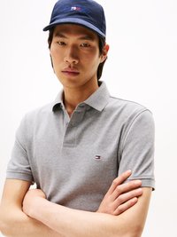Grijze polo met korte mouwen, voorzien van een klein gekleurd logo op de borst. Het model draagt een donkerblauwe pet met een logo.