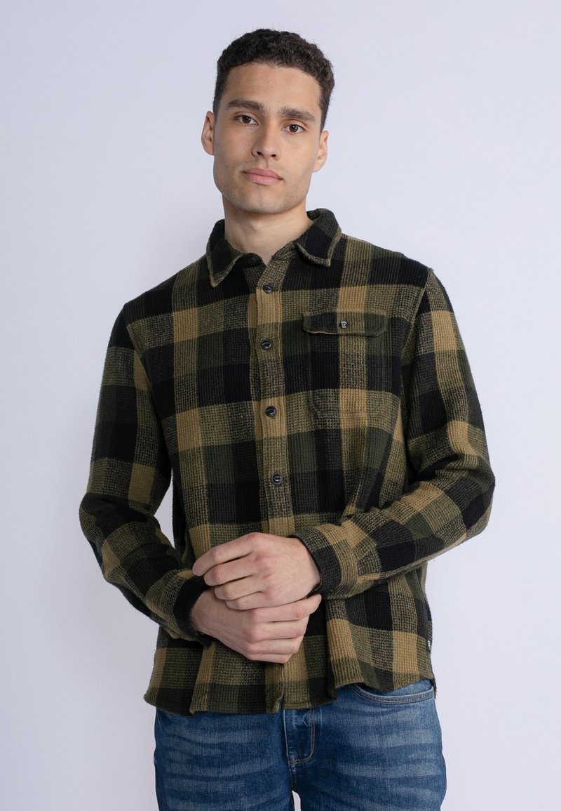 Karierte Flanellhemd mit schwarzer, grüner und brauner Farbe; verfügt über eine Knopfleiste, einen Kragen und eine einzelne Brusttasche. Weicher Textur.