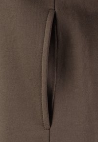 Tejido marrón con textura acanalada, que presenta un detalle de bolsillo vertical con abertura. El diseño es elegante y ajustado para una apariencia aerodinámica.