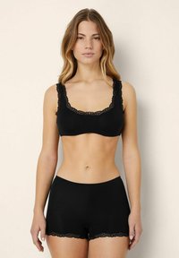 Černý krajkový bralette a odpovídající kalhotky typu boyshorts. Látka je měkká s hladkým povrchem a má krajkový lem kolem okrajů obou kousků.