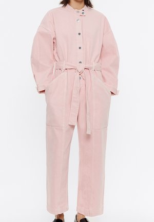Pink denim jumpsuit with long sleeves, button closure, belt at waist, and two front pockets; relaxed fit with visible stitching details.