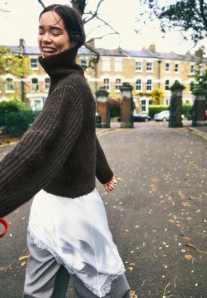 Pulover maro cu dungi, guler înalt, asortat cu o fustă albă cu dantelă la margine și pantaloni gri; decor exterior cu frunze de toamnă.