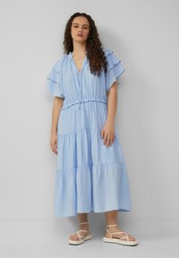 Himmelblaues, gestuftes Maxikleid mit Rüschensleeves und Kordelzug in der Taille. Getragen mit flachen, geschnürten Sandalen. Glattes, leichtes Material.