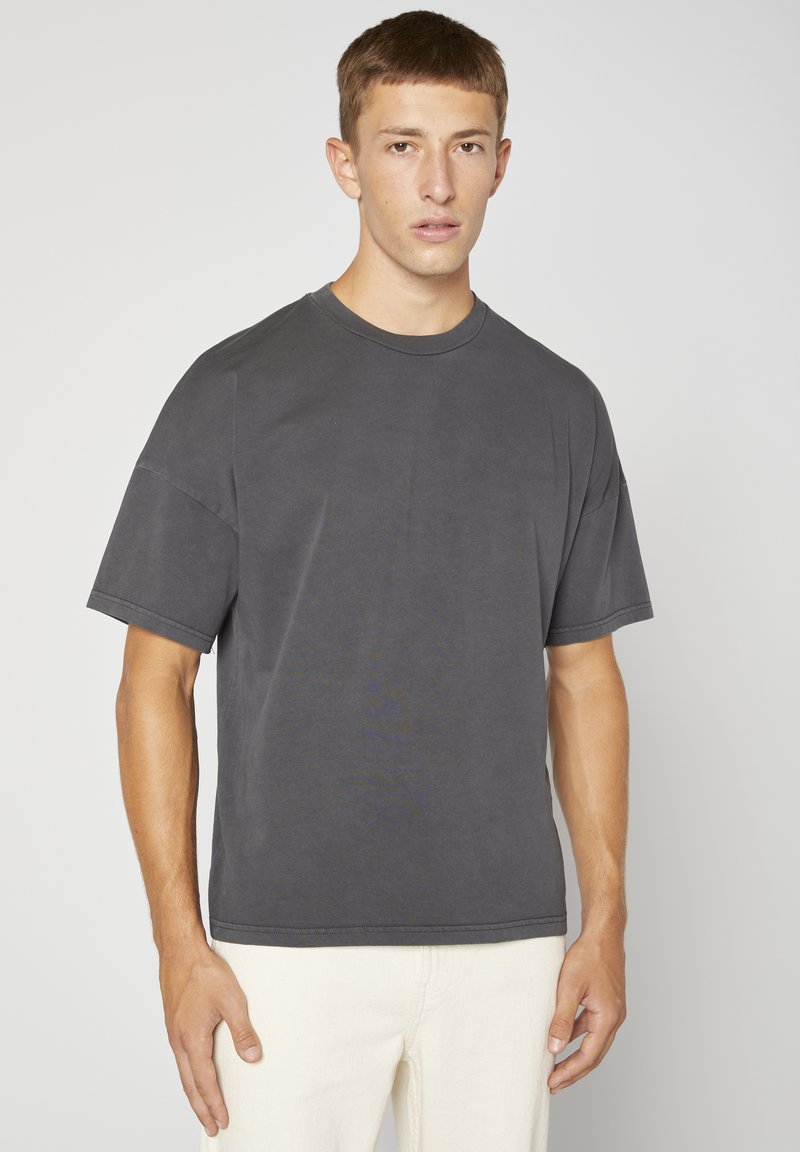 T-shirt grise surdimensionné en coton doux avec un col rond et des manches courtes. Présente des coutures doubles et une coupe décontractée.