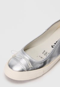 Silberne metallische Ballerinas mit weißer Gummisohle und kleiner Schleife auf der runden Zehenpartie, die einen Teil des inneren beigen Futters zeigt.