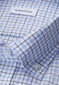 Collare di camicia a quadri blu e bianchi con una texture in cotone, dotato di un'etichetta recante la scritta "seidensticker" e bottoni in plastica trasparente.