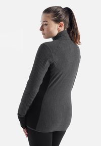 Maglia sportiva a maniche lunghe di colore grigio scuro con tessuto texture, colletto alto e dettagli neri. Progettata per una silhouette aderente.