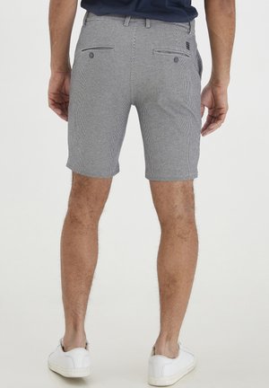 Harmaa ja valkoinen raitashortsit, joissa on muotoiltu malli, etu- ja takataskut sekä vyötärönauha. Yhdistetty valkoisiin lenkkareihin.