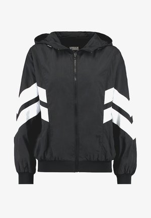 Juodas vėjinės striukės vėjaraštis su priekiniais užtrauktukais, kapisonu ir elastinėmis rankovėmis. Yra baltos įstrižinės juostos ant rankovių kontrastui.