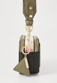 Sac zippé compact noir et vert olive avec un porte-clés doré, en tissu texturé, et un charm triangulaire. Comprend trois compartiments zippés.