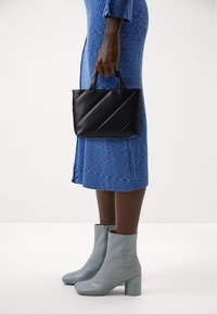Black leather handbag with diagonal quilting and two handles, paired with a blue ribbed dress and light blue heeled ankle boots.