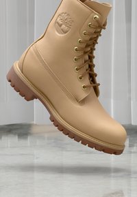 Botte en cuir tanné avec une finition texturée, œillets en or et semelle en caoutchouc marron. Présente un logo en relief sur le côté externe.