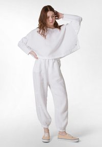 Witte linnen oversized top met brede mouwen, gecombineerd met witte linnen joggers met elastische manchetten. Model draagt beige sneakers.