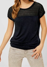 Námořnická modrá tričko s texturovaným černým síťovaným vrškem, krátkými rukávy a volným střihem. Hladká látka s jemným leskem a vzorem herringbone.