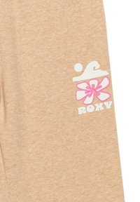 Beige tyg med en mjuk textur har ett vitt vågmönster och en rosa blommig design bredvid ordet "ROXY" i vita bokstäver.