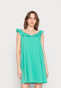 Vestido verde sem mangas, feito de tecido suave, com um decote franzido e uma silhueta em A que cai acima do joelho.