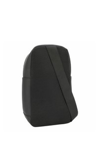 Zaino nero con materiale a rete, design angolato, tracolla regolabile e dettagli lisci. Forma compatta e moderna con dettagli minimi.