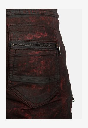 Black denim with a distressed red pattern, featuring a zippered back pocket and textured fabric. Clean lines and a rugged appearance.
