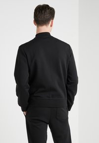 Svart sweatshirt med rund halsringning och ribbade muddar, med en mjuk yta. Baksidan visar en minimalistisk design utan mönster.