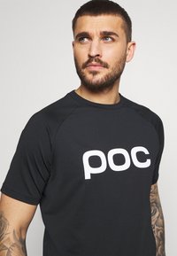 Černé sportovní tričko s bílým logem "poc". Krátké rukávy, raglánový design a hladká textura pro snadný pohyb.
