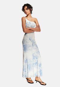 Ett tvådelat set bestående av en ljusblå blommig crop top med spagettiband och en matchande lång kjol med veck och en flytande design.