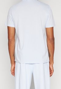 Jasnoniebieska bawełniana koszulka z krótkimi rękawami, okrągłym dekoltem i luźnym krojem. Gładka faktura bez widocznych wzorów czy zdobień.